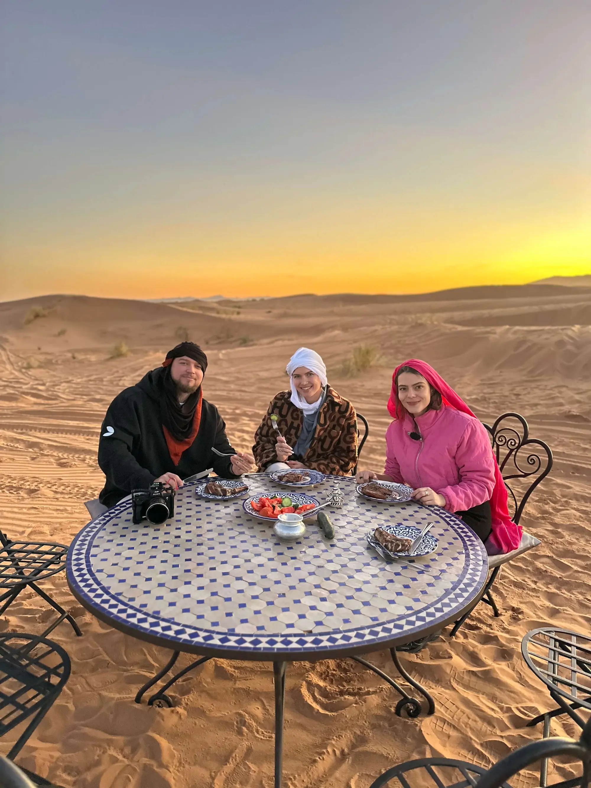 Traditional Moroccan outdoor dining set on the Sahara dunes during golden hour for a private tour group.